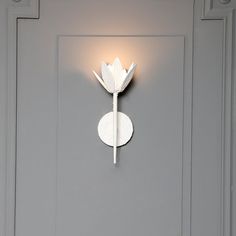 a white wall mounted light on the side of a gray door with a single flower