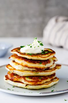 a stack of pancakes topped with whipped cream and parsley on a white plate next to a blue bowl