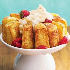 a cake with strawberries and whipped cream on top sits on a white pedestal in front of a blue wall