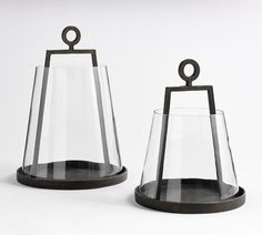 two glass vases sitting on top of each other next to each other, one with a metal handle