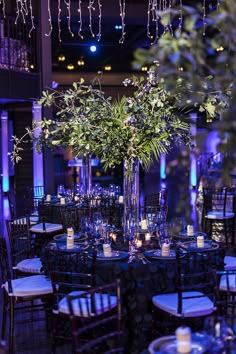 a tall vase filled with flowers and greenery on top of a table surrounded by chairs