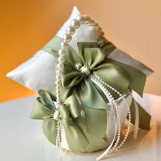 a ring pillow with pearls and green ribbon on the front is sitting on a table