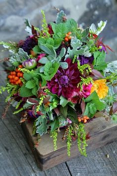 a bouquet of flowers sitting on top of a wooden box filled with leaves and berries