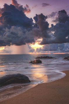 the sun is setting over the ocean with clouds in the sky and rocks on the beach