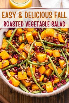 a white bowl filled with roasted vegetables and green beans next to a glass of orange juice