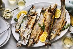 fish and lemons are served on a white plate with silverware next to wine glasses