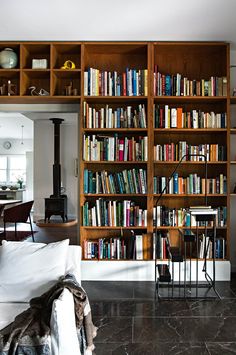 a living room filled with lots of books on top of a wooden book shelf next to a white couch