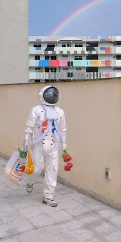 a man in an astronaut suit walking down a sidewalk with a rainbow in the background