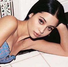 a beautiful young woman laying on top of a white tile floor next to a wall