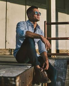 a man sitting on top of a wooden bench next to a metal rail and wearing sunglasses