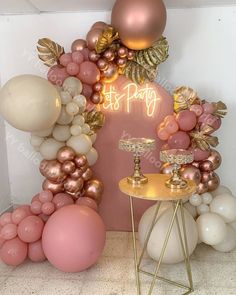 a table topped with lots of balloons next to a pink and gold arch that says it's party