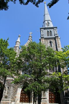 an old church with steeple and trees in the foreground