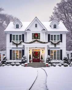 a large white house with wreaths and lights on it's front door in the snow