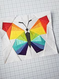 a colorful butterfly made out of paper sitting on top of a piece of white fabric