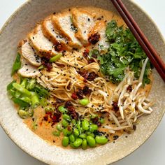 a bowl filled with noodles, meat and veggies next to chopsticks