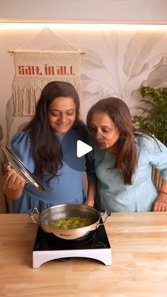 two women standing in front of a stove preparing food on top of a wooden table