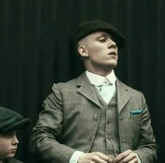 a man wearing a suit and tie with his hands in his pockets while standing against a black background