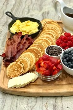 the breakfast is ready to be eaten on the wooden platter with fruit, eggs, bacon and pancakes