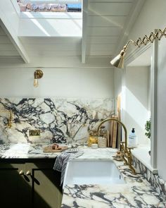 a kitchen with marble counter tops and gold faucet lights above the sink in front of an open skylight