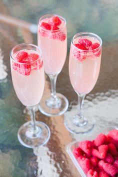 three wine glasses filled with raspberries on a table next to some strawberries