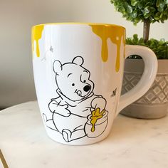 a winnie the pooh coffee mug sitting on top of a table next to a potted plant