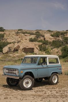 an old blue pick up truck parked in the middle of a field with rocks behind it