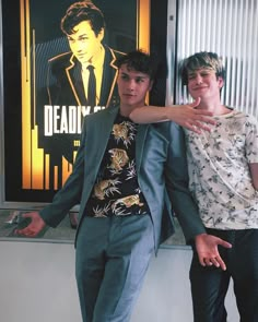 two young men standing next to each other in front of a wall with a movie poster behind them