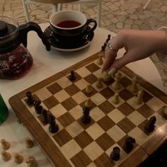 a person playing chess on a table with a cup of tea and kettles in the background