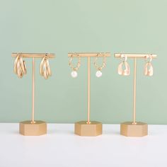 three gold jewelry stands with earrings hanging from the hooks on each one, and two different sized earring holders