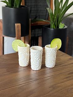 three shot glasses sitting on top of a wooden table next to potted plantes