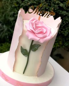 a pink rose is on top of a white cake with gold lettering and a name