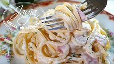 a fork is stuck into some pasta with ham and cheese on it, in a floral plate