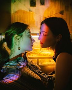 two young women sitting next to each other in front of a light filled room with yellow lights