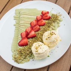 a white plate topped with sliced strawberries and ice cream on top of a wooden table