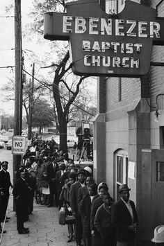 an old black and white photo of people standing in front of a baptist church sign