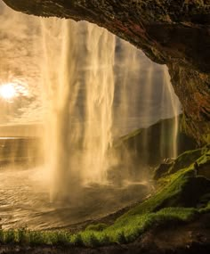 the sun shines through an opening in a cave with water cascading from it