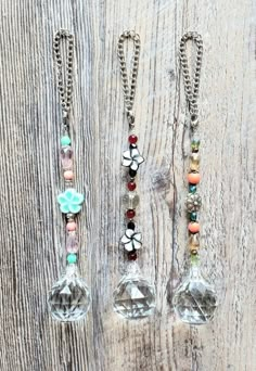 three necklaces with charms hanging from them on a wooden surface and one has a flower in the center