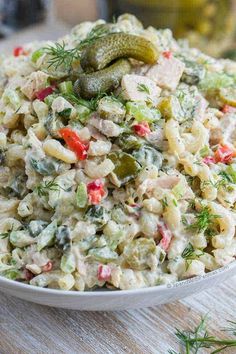 a white bowl filled with pasta salad on top of a wooden table next to a pickle