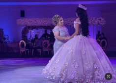 two women in gowns standing next to each other on a stage with purple lighting