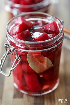 two jars filled with pickled fruit on top of a wooden table next to utensils