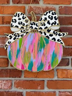 a painted pumpkin hanging on the side of a brick wall with a leopard print bow