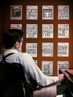 a man sitting at a desk in front of a black and white wall with posters on it