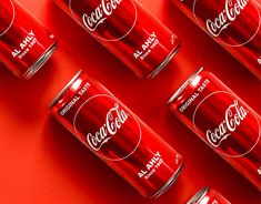 six cans of coca - cola are lined up on a bright red surface, with the lids slightly open