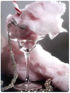 a pink cotton candy in a glass next to a necklace and a candle on a table