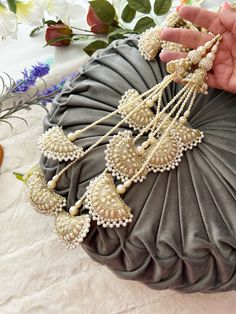 a hand is holding some white beads on a gray pillow with flowers in the background