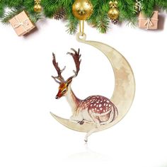 a christmas ornament with a deer sitting on the moon and presents under it