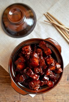 a brown bowl filled with food next to chopsticks and a cup on top of a wooden table