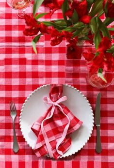 a red and white checkered table cloth with silverware on it next to flowers