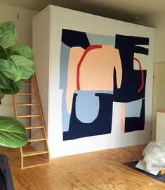 a painting on the wall next to a plant and some stairs in a room with hard wood flooring