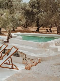 an outdoor swimming pool surrounded by trees and stone steps with chairs next to the pool